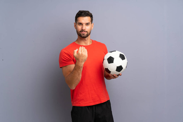 Handsome young football player man over isolated white wall inviting to come with hand. Happy that you came - Foto, afbeelding