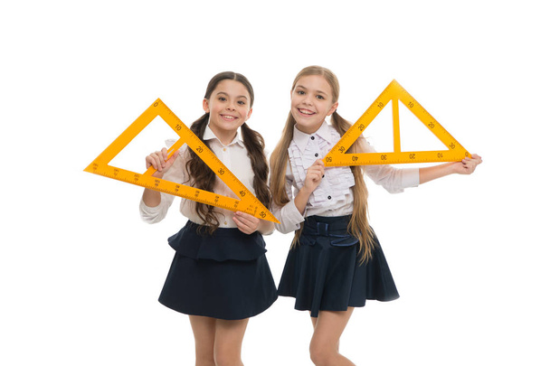 Our geometry lesson for the day. Cute schoolgirls holding triangular rulers for lesson. Small children with measuring instruments at school lesson. Little girls preparing for geometry lesson - Photo, image