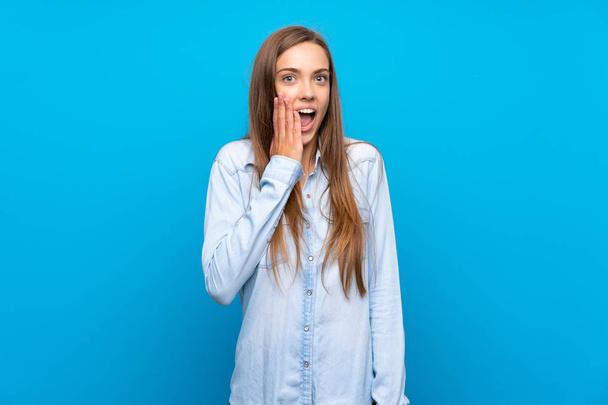 Νεαρή γυναίκα πάνω από απομονωμένο μπλε φόντο με έκπληξη και σοκαρισμένη έκφραση προσώπου - Φωτογραφία, εικόνα