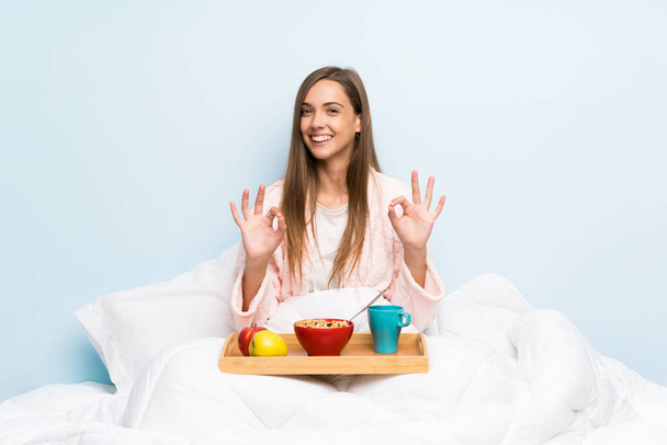 Молодая женщина в халате с завтраком показывает знак ОК с пальцами
 - Фото, изображение