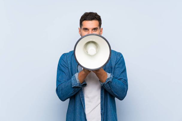 Handsome man over isolated blue background shouting through a megaphone - Photo, Image