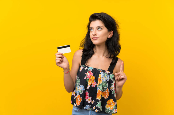Young woman over isolated yellow background holding a credit card - Photo, Image