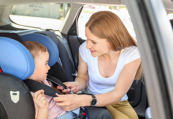 Madre abrochando a su pequeño hijo en el asiento del coche
 - Foto, imagen