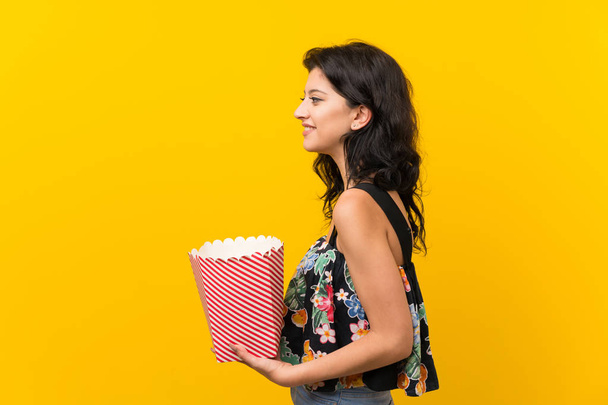 Young woman over isolated yellow background holding a bowl of popcorns - 写真・画像