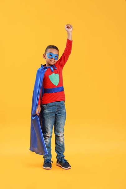 色の背景にスーパーヒーローの服を着たかわいいアフリカ系アメリカ人の少年 - 写真・画像