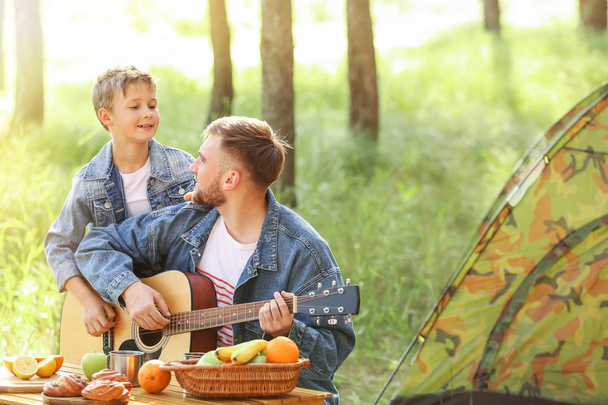 Vater und sein kleiner Sohn mit Gitarre picknicken im Wald - Foto, Bild