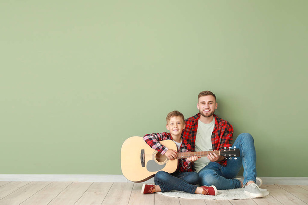 Портрет щасливого батька і сина з гітарою, що сидить біля кольорової стіни
 - Фото, зображення