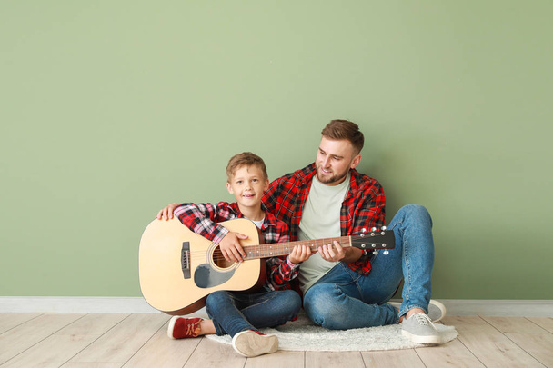 Portret szczęśliwego ojca i syna z gitarą siedzącą w pobliżu kolorowej ściany - Zdjęcie, obraz