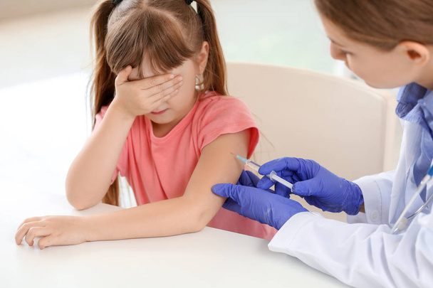 クリニックで小さな女の子にワクチンを接種する医師 - 写真・画像
