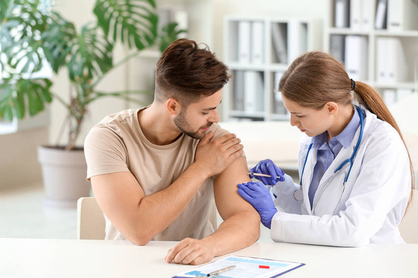Doctor vaccinating young man in clinic - Photo, image