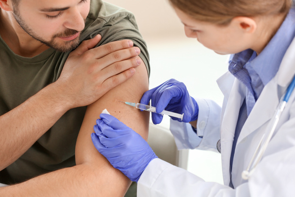 クリニックで若い男性にワクチンを接種する医師 - 写真・画像