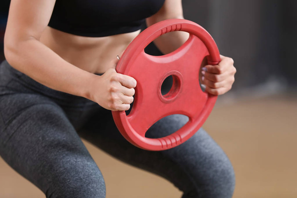 Sporty young woman training with weight plate in gym - Photo, Image