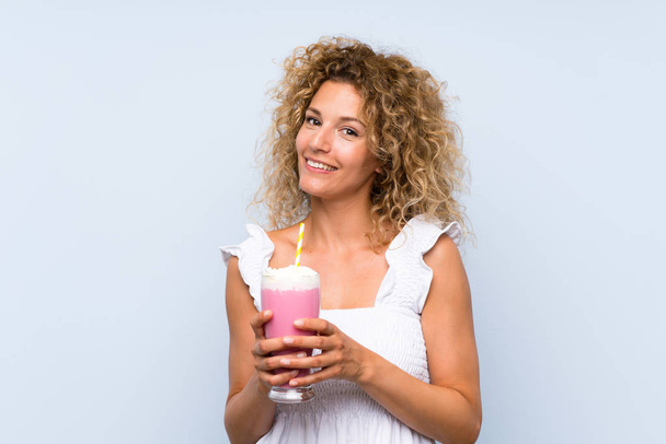 Young blonde woman with curly hair holding a strawberry milkshake - Foto, Imagem