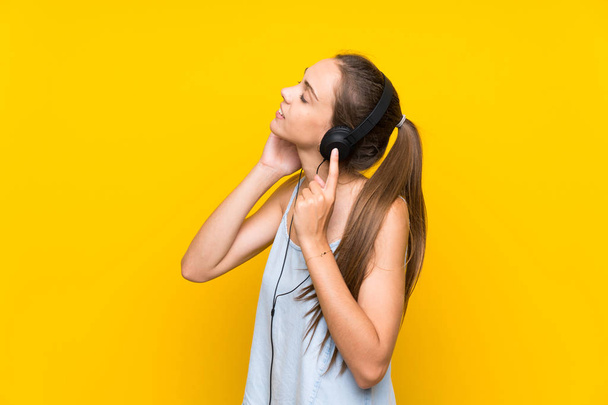 Fiatal nő hallgat zenét az elszigetelt sárga fal - Fotó, kép