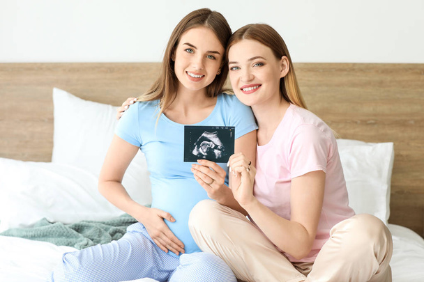 Schwangere lesbisches Paar mit Sonogramm-Bild im Schlafzimmer - Foto, Bild