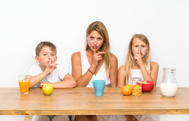 Мама с двумя детьми завтракает и делает жест молчания
 - Фото, изображение