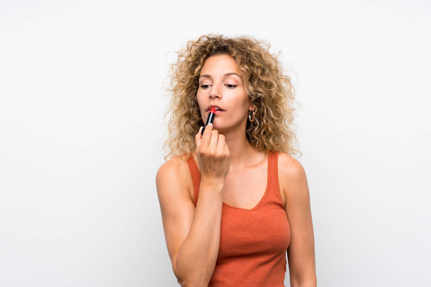 Jonge blonde vrouw met krullend haar houdt rode lippenstift - Foto, afbeelding