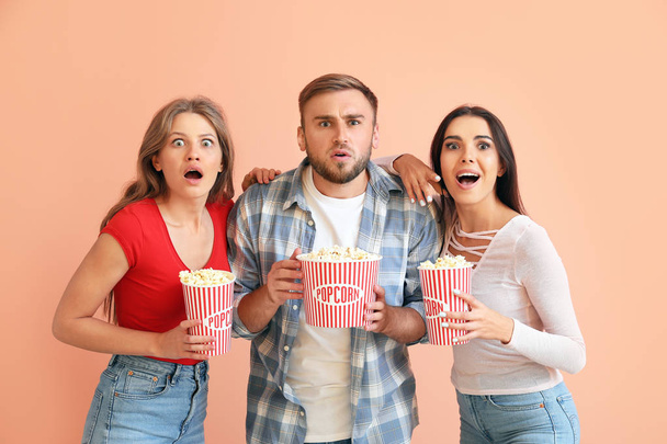 Emotional friends with popcorn watching horror movie on color background - Foto, afbeelding