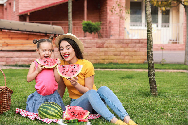 Милая маленькая девочка и ее мать едят сладкий арбуз в парке
 - Фото, изображение