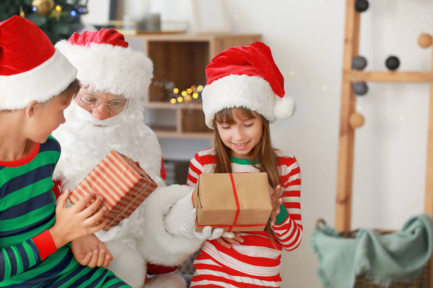 Weihnachtsmann und seine kleinen Helfer mit Geschenken im weihnachtlich dekorierten Raum - Foto, Bild