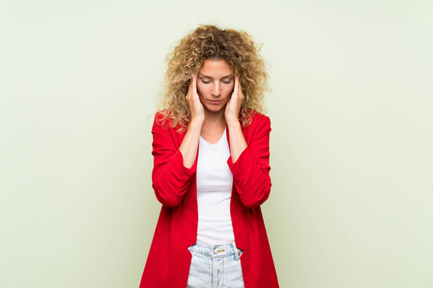 Young blonde woman with curly hair over isolated green background with headache - Fotoğraf, Görsel