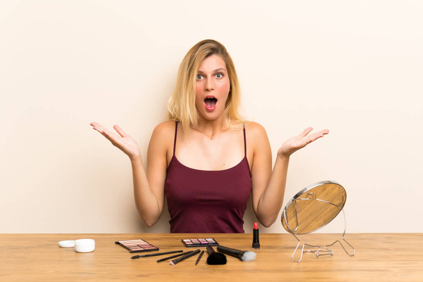 Mladá blondýnka s kosmetickým výrazem v stolku s překvapením na tváři - Fotografie, Obrázek