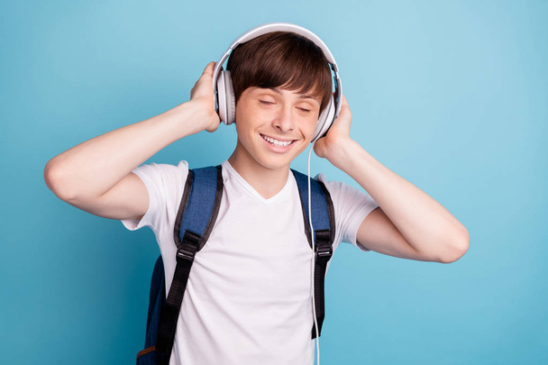 Photo of rejoicing overjoyed boy deepened into world of music while isolated with blue background - Foto, afbeelding