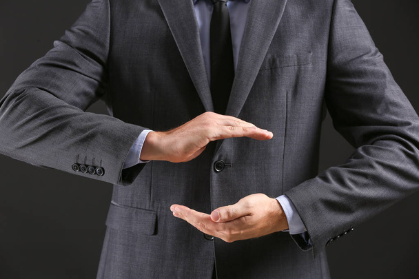 Businessman holding something against dark background, closeup - Photo, Image