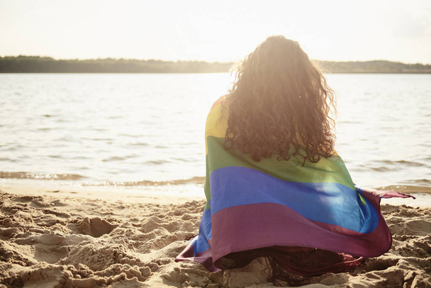 Achteraanzicht van de jonge vrouw bedekt met regenboog vlag  - Foto, afbeelding