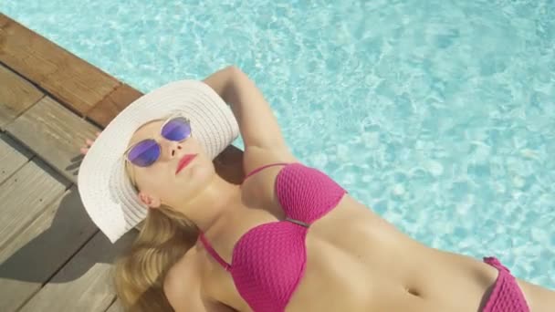 Slow Motion, close-up, kopieer ruimte: jonge blonde vrouw met aantrekkelijke lange benen slaapt bij het zwembad. Gelukkig badpak model genieten van de aangename zomer zonnestralen tijdens het nemen van een dutje door een luxe zwembad. - Video