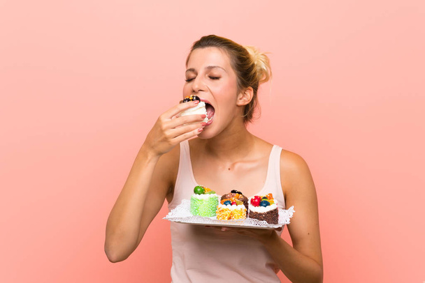 Young blonde woman holding lots of different mini cakes - Photo, Image