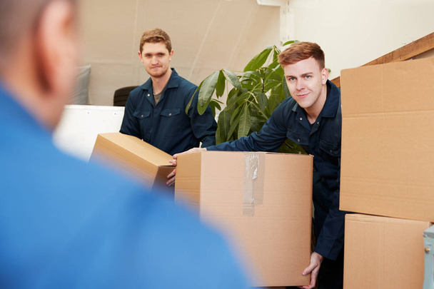 Removal Company Workers Unloading Furniture And Boxes From Truck Into New Home On Moving Day - 写真・画像