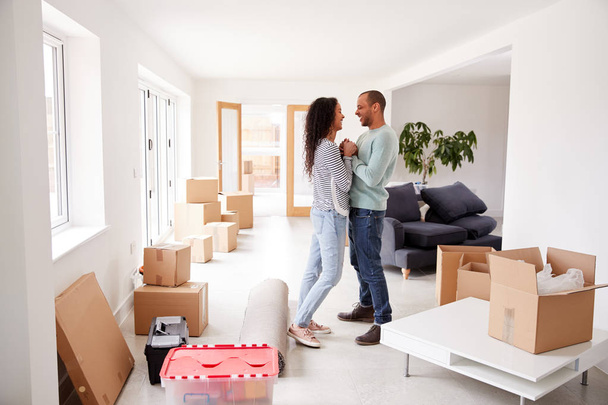 Loving Couple Surrounded By Boxes In New Home On Moving Day - Фото, изображение