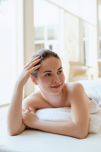 Beautiful young woman relaxing in the spa salon on light background. Massage. Body care. Spa body. Cosmetology. - 写真・画像