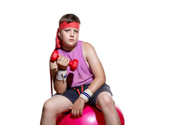 het kind zit op een roze fitbal in een roze trainingspak en met een pleister op zijn hoofd en treinen biceps - Foto, afbeelding