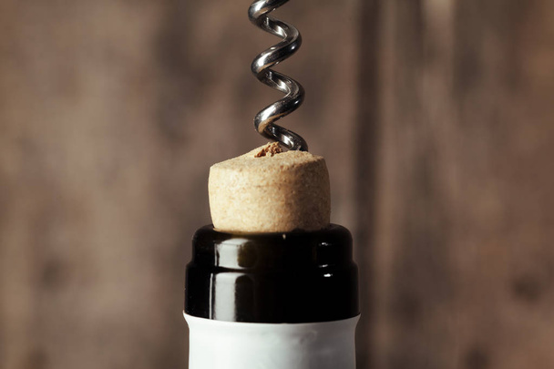 Bottle of wine with corkscrew on wooden background - Fotó, kép