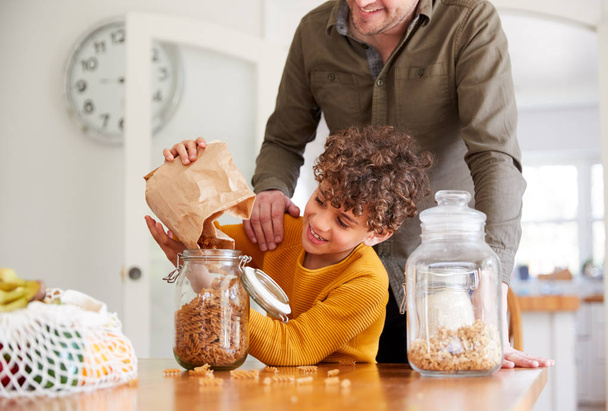Father Helping Son To Refill Food Containers At Home Using Zero Waste Packaging - 写真・画像