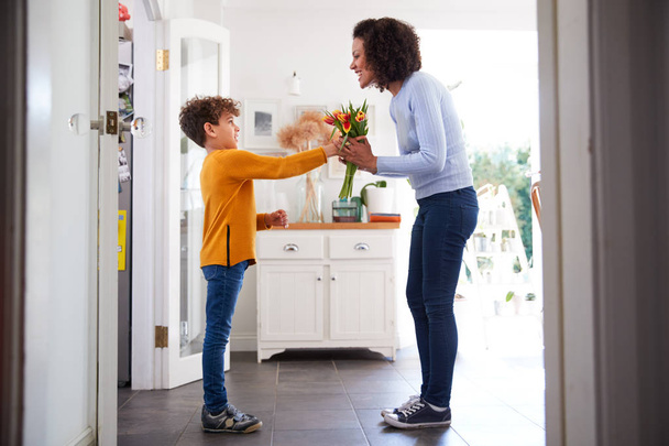Loving Son Giving Mother Bunch Of Flowers To Celebrate Mothers Day At Home - Фото, зображення