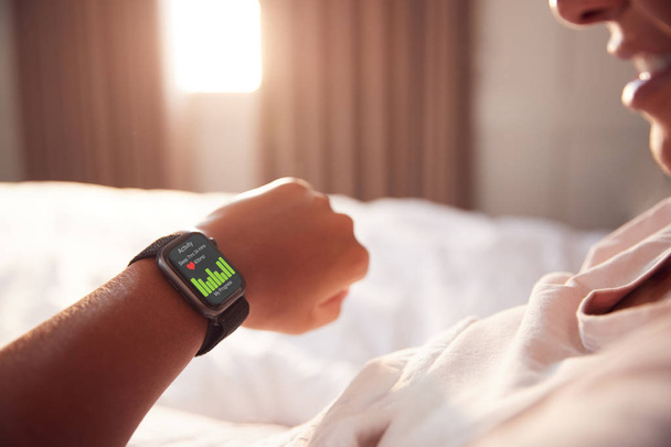 Woman Sitting Up In Bed Looking At Screen Of Smart Watch - Foto, imagen