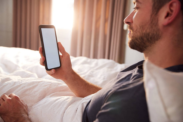 Man Sitting Up In Bed Looking At Mobile Phone After Having Woken Up - Photo, image
