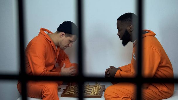 African american and caucasian criminals playing chess in cell, hobby in prison - Фото, изображение