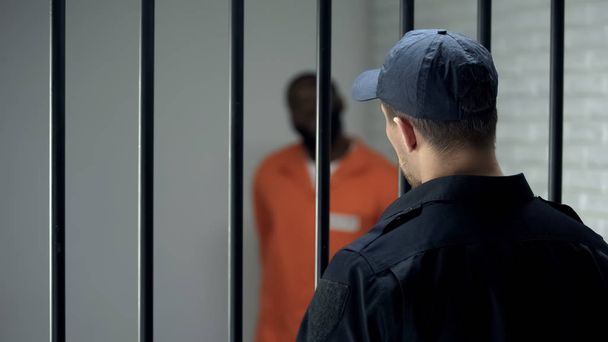 Warden looking at dangerous criminal standing in cell, life sentence, prison - 写真・画像