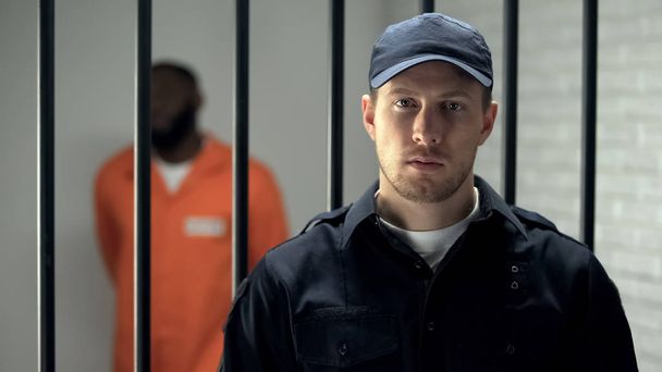 Warden looking at camera in prison, african american criminal on background - Zdjęcie, obraz