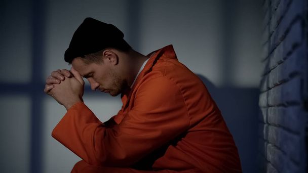 Caucasian imprisoned male praying in cell, feeling guilty and asking for mercy - Fotó, kép