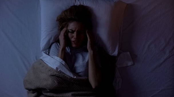 Woman suffering from terrible headache lying in bed at night, life in big city - Foto, afbeelding