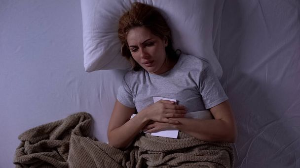 Upset woman crying in bed, holding divorce certificate, pain of husband loss - Foto, immagini