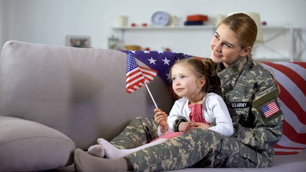 American female veteran and little daughter with flag watching military march - Фото, зображення