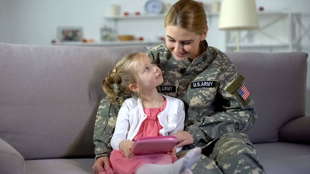 Mother in US army uniform and little daughter playing game on tablet together - Photo, Image