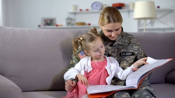 Female soldier and cute daughter watching pictures in coloring book leisure time - Photo, Image