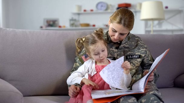 Mom in military uniform looking at drawings in coloring book together, leisure - Fotografie, Obrázek